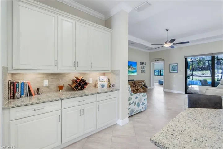 Kitchen with crown molding, light stone counters, white cabinetry, ceiling fan, and decorative backsplash