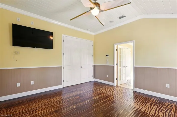 Unfurnished bedroom featuring a wainscoted wall, hardwood / wood-style flooring, ornamental molding, a closet, and baseboards