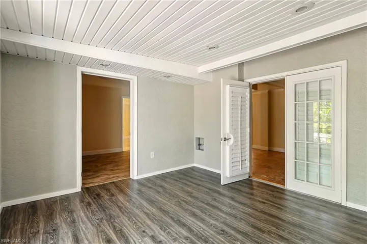 Unfurnished room featuring a textured wall, dark wood-type flooring, wooden ceiling, baseboards, and french doors