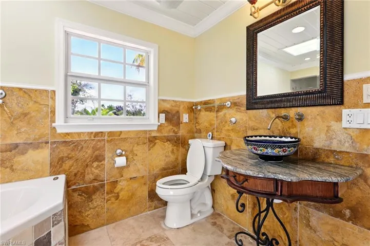 Full bathroom with ornamental molding, tile walls, toilet, a sink, and tiled tub