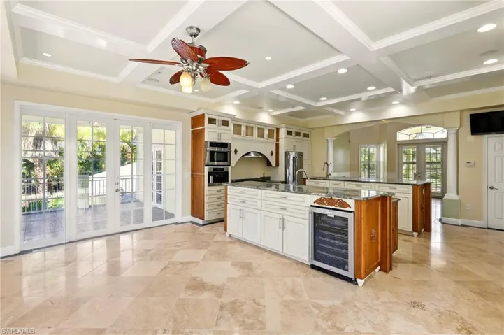 Kitchen with wine cooler, coffered ceiling, a large island, decorative columns, and french doors
