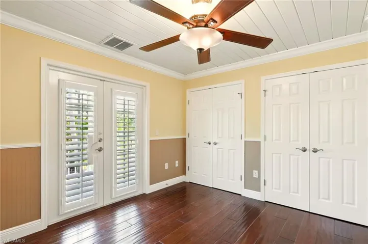 Unfurnished bedroom featuring multiple closets, access to outside, ornamental molding, wainscoting, and dark wood finished floors