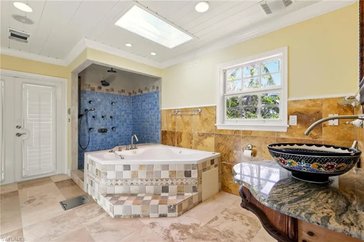 Full bath with a skylight, ornamental molding, tile walls, a sink, and a bath