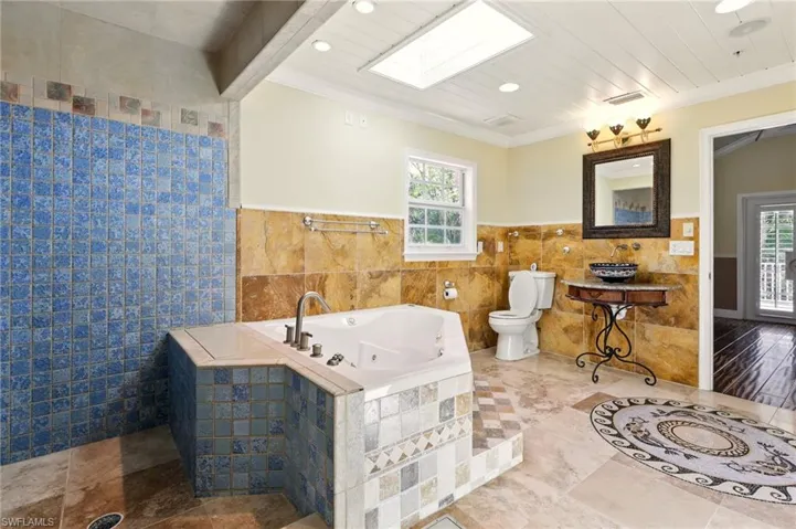 Full bath with tile walls, toilet, ornamental molding, plenty of natural light, and a jetted tub