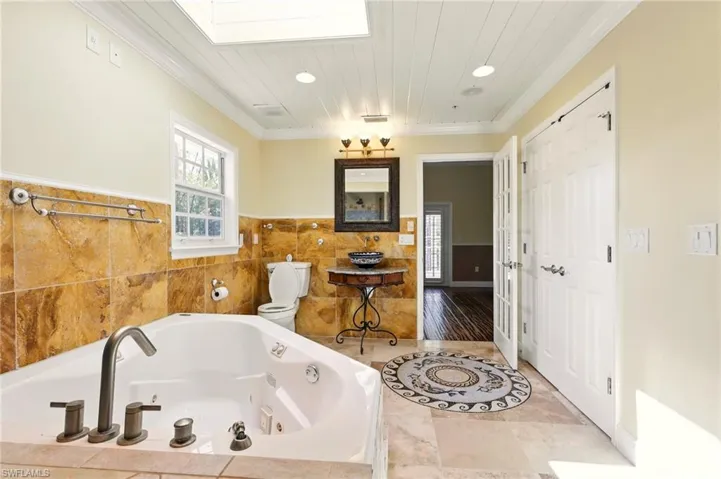 Bathroom featuring toilet, a whirlpool tub, tile walls, crown molding, and recessed lighting