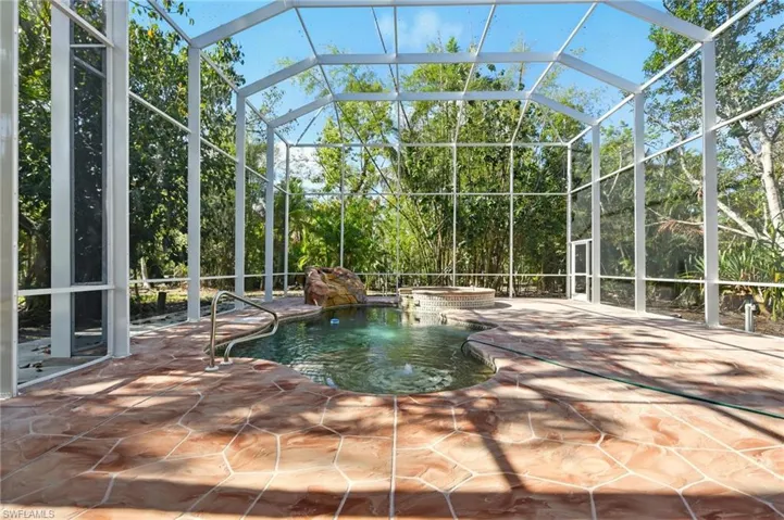 View of pool featuring a patio area, glass enclosure, and a pool with connected hot tub