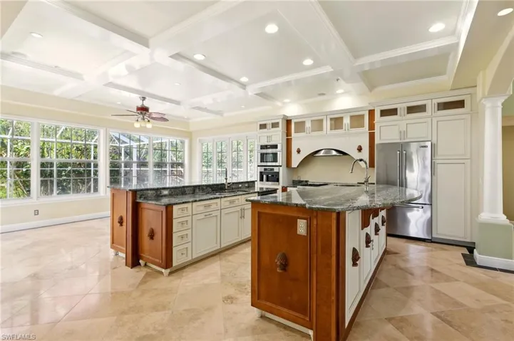 Kitchen with high end fridge, a center island with sink, ornate columns, coffered ceiling, and a ceiling fan