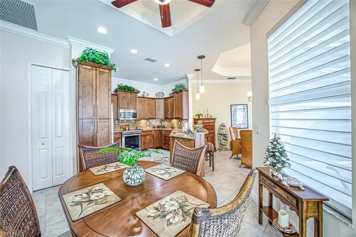 Tiled dining area featuring a tray ceiling, sink, ceiling fan, and ornamental molding