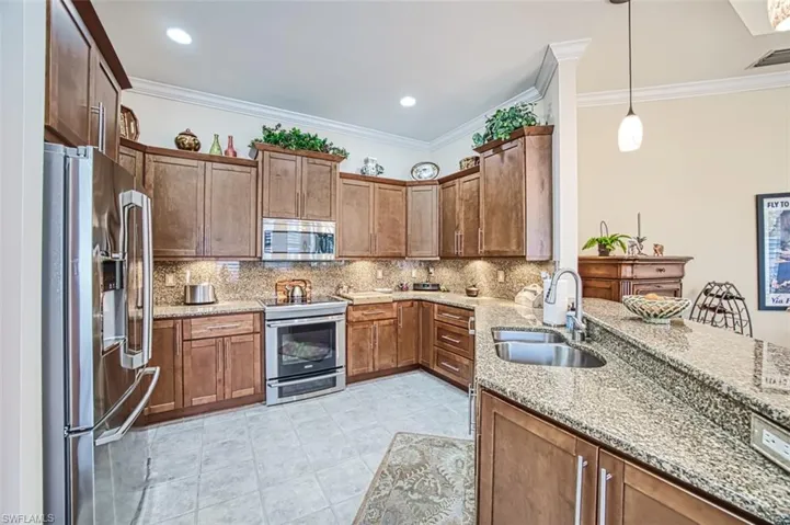 Kitchen featuring light tile patterned floors, stainless steel appliances, light stone countertops, pendant lighting, and sink