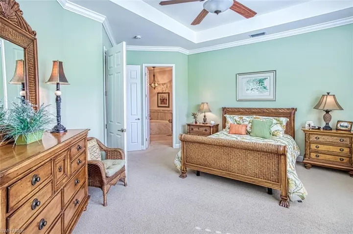 Carpeted bedroom with ensuite bath, a tray ceiling, ceiling fan, and ornamental molding