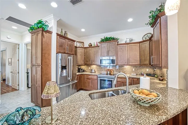 Kitchen with appliances with stainless steel finishes, kitchen peninsula, decorative backsplash, light wood-type flooring, and ornamental molding