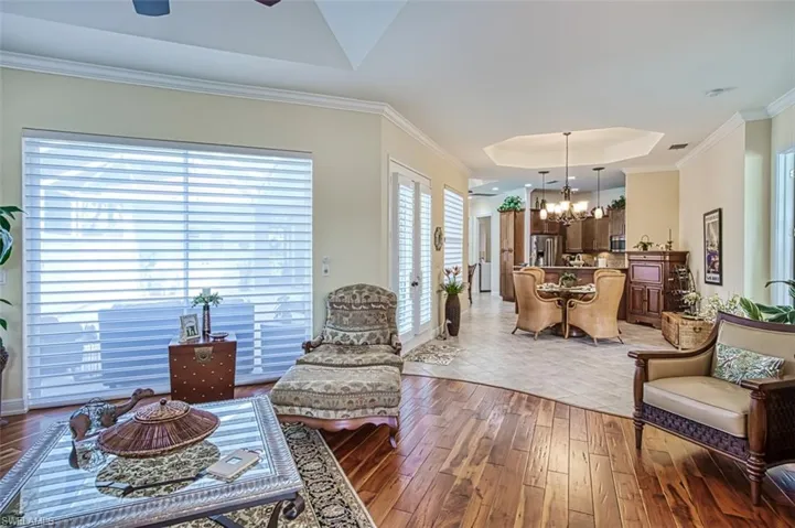 Living room with a healthy amount of sunlight, ceiling fan with notable chandelier, a raised ceiling, and tile patterned floors