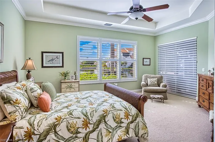 Carpeted bedroom featuring a tray ceiling, ceiling fan, and ornamental molding