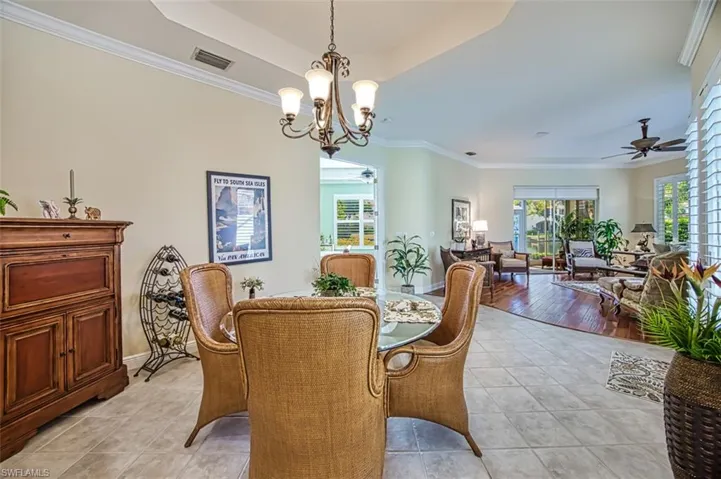 Tiled dining room with ceiling fan with notable chandelier, crown molding, and a raised ceiling
