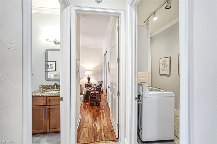 Corridor with rail lighting, ornamental molding, sink, washer / dryer, and light hardwood / wood-style floors