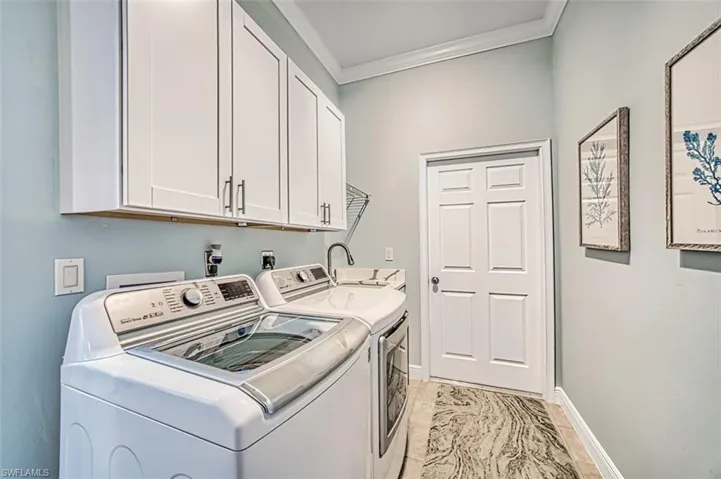 Laundry room with crown molding, sink, washer and dryer, cabinets, and light tile patterned floors