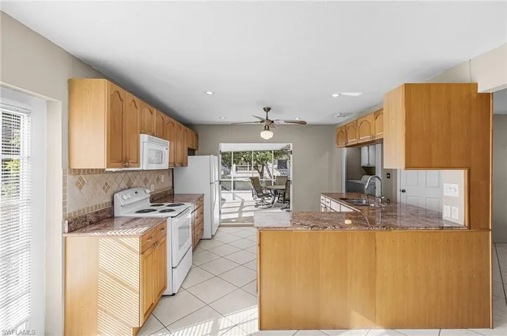 Kitchen with white appliances, a peninsula, backsplash, a ceiling fan, and light tile patterned flooring