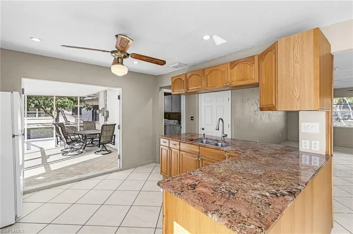 Kitchen with ceiling fan, freestanding refrigerator, dark stone countertops, light tile patterned floors, and a peninsula