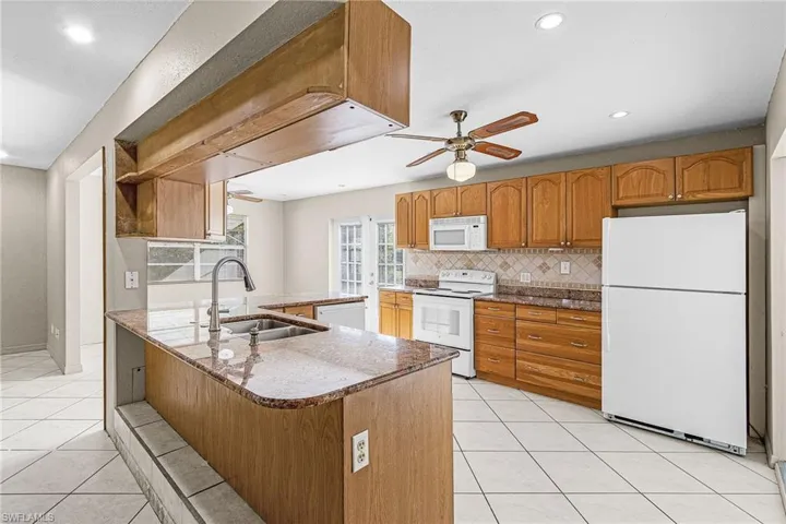 Kitchen featuring wood finish cabinets, light tile patterned floors, white appliances, a peninsula, and dark stone counters