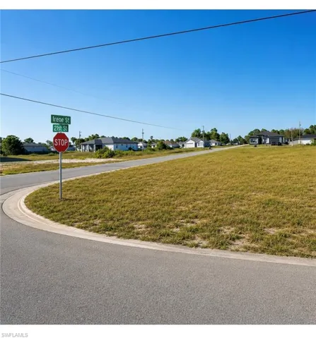 Grassed lot featuring a paved road frontage, concrete curb, and street signage