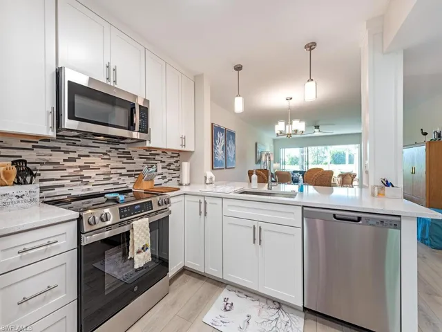 Kitchen with appliances with stainless steel finishes, white cabinets, open floor plan, and hanging light fixtures