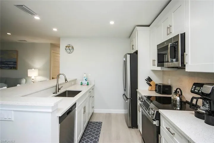 Kitchen featuring white cabinets, a peninsula, light stone counters, stainless steel appliances, and recessed lighting