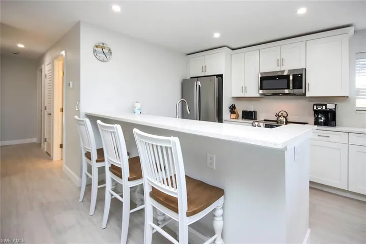 Kitchen featuring a breakfast bar, white cabinets, stainless steel appliances, a peninsula.