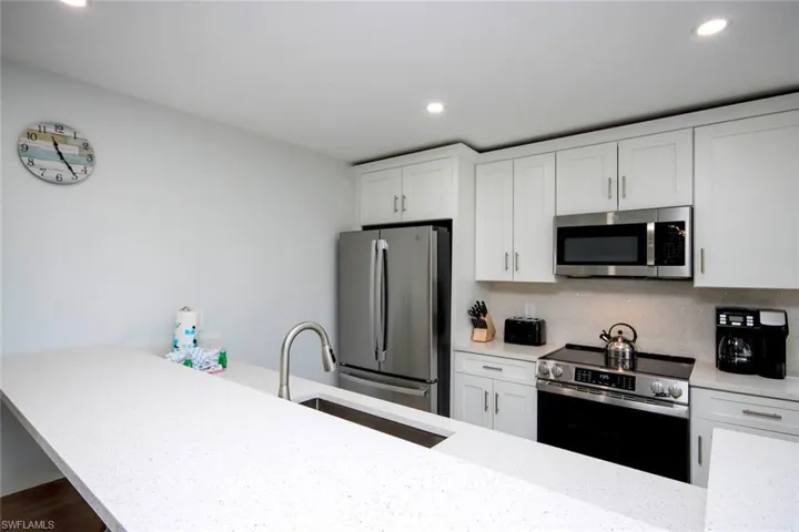 Kitchen with stainless steel appliances, light stone counters, white cabinetry, tasteful backsplash, and recessed lighting