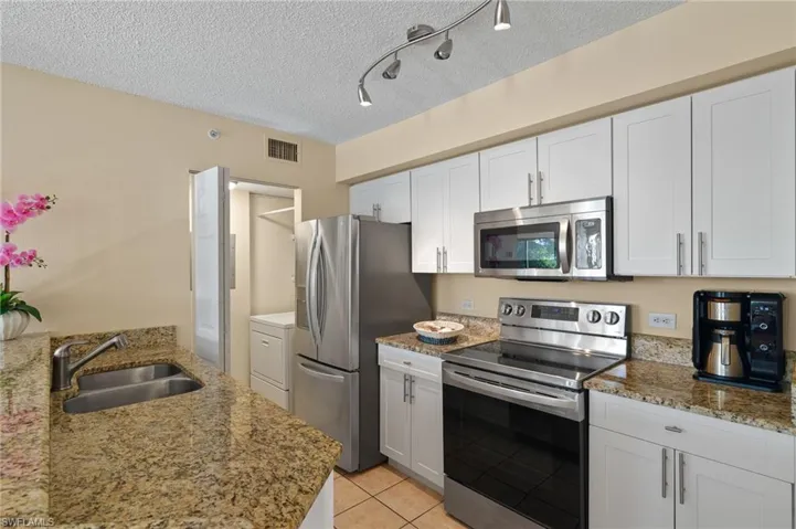 Kitchen with rail lighting, a textured ceiling, white cabinets, appliances with stainless steel finishes, and sink