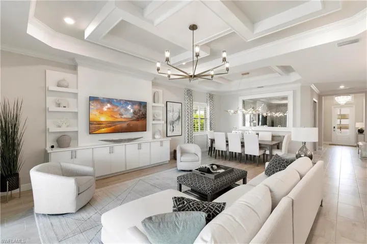 Tiled living room with a wealth of natural light, tray ceiling, crown molding, coffered ceiling, and an inviting chandelier