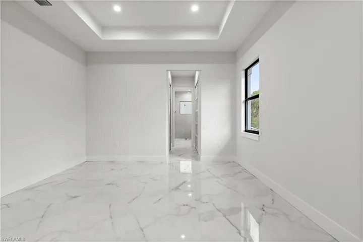 Spare room with a raised ceiling, light marble finish floors, and recessed lighting