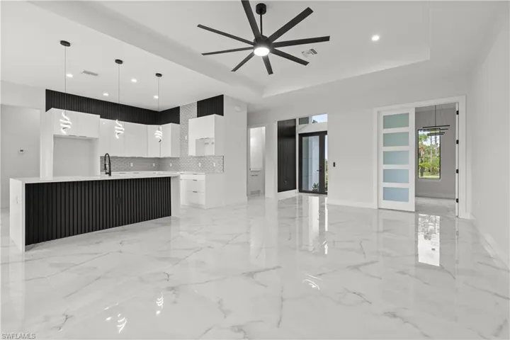 Unfurnished living room featuring a ceiling fan, a tray ceiling, recessed lighting, and light marble finish floors