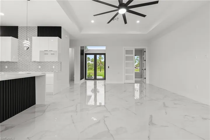 Unfurnished living room featuring a ceiling fan, a raised ceiling, light marble finish flooring, and recessed lighting