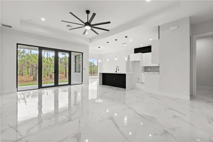 Unfurnished living room with a tray ceiling, ceiling fan, light marble finish floors, recessed lighting, and french doors