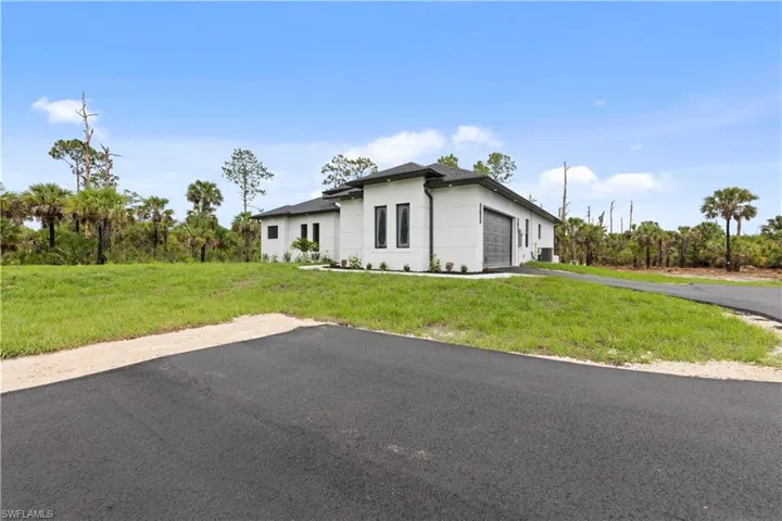 View of front of home with an attached garage, driveway, a front lawn, and stucco siding