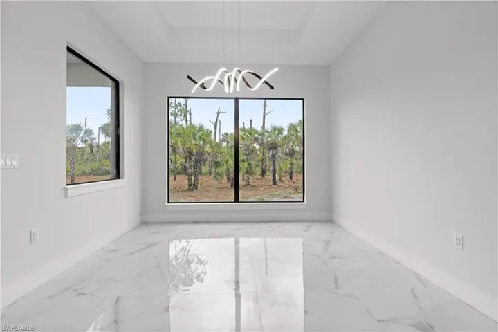 Empty room with marble finish flooring, a chandelier, and a tray ceiling