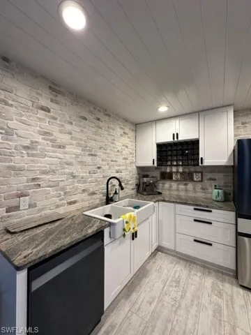 Kitchen with dark stone countertops, white cabinets, dishwasher, fridge, and sink