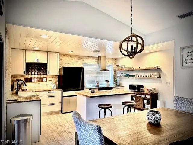 Kitchen featuring black refrigerator, decorative backsplash, sink, exhaust hood, and a kitchen bar