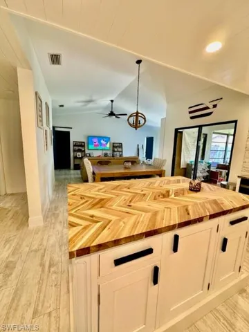 Kitchen featuring light wood-type flooring, wood counters, decorative light fixtures, and white cabinets