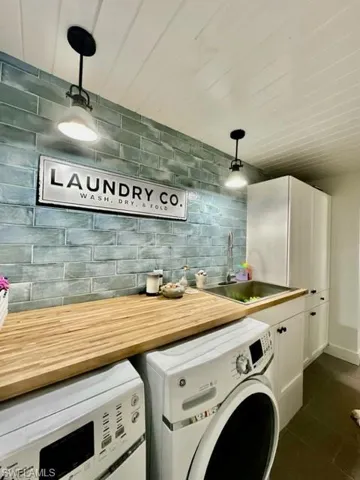 Laundry room with sink, washing machine and dryer, dark tile patterned floors, and cabinets