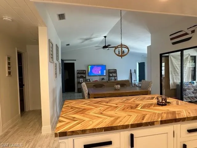 Kitchen with wooden counters, white cabinetry, vaulted ceiling, and ceiling fan
