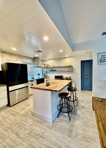 Kitchen with stainless steel refrigerator, a kitchen island, light hardwood / wood-style floors, wall chimney exhaust hood, and butcher block countertops