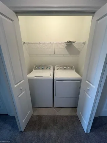 Washroom with light colored carpet, light tile patterned floors, and washer and dryer