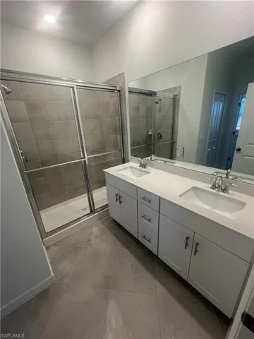 Bathroom featuring double vanity, a stall shower, and light tile patterned floors