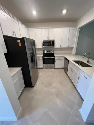Kitchen with stainless steel appliances, white cabinetry, recessed lighting, light tile patterned flooring, and light stone countertops