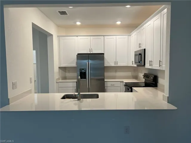 Kitchen featuring white cabinetry, stainless steel appliances, light stone counters, and recessed lighting