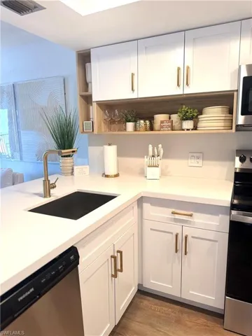 Kitchen featuring stainless steel appliances, a sink, white cabinetry, light countertops, and open shelves