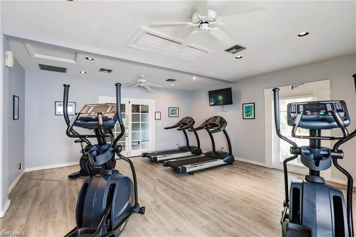 Workout area featuring light wood-style floors, baseboards, visible vents, and a ceiling fan