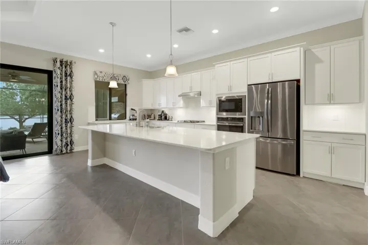 Light & bright kitchen with recessed & pendant lighting, a large island and stainless steel appliances