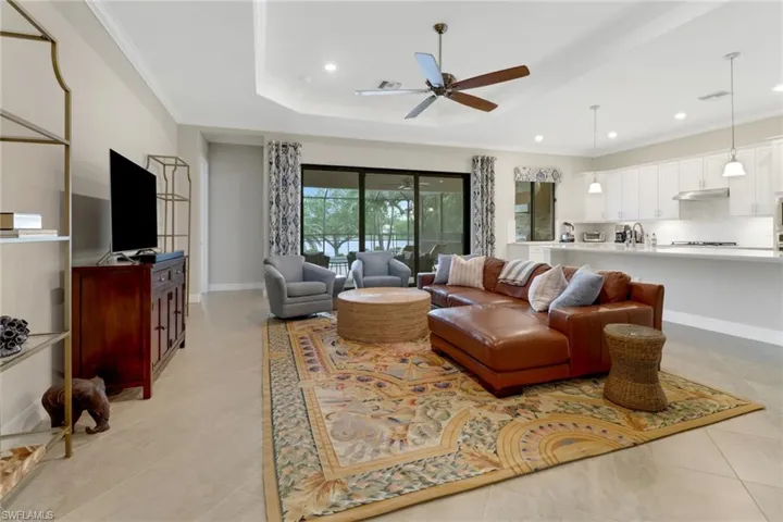 Tiled great room featuring tray ceiling, ceiling fan, and sliding glass door leading to the lanai